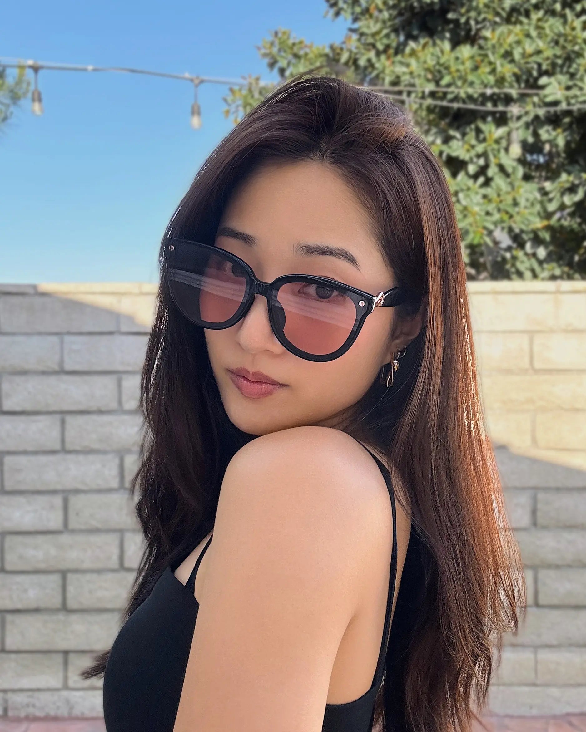 Woman wearing Sweet Pain NANA C1 sunglasses in glossy black with citrus lens, outdoor selfie
